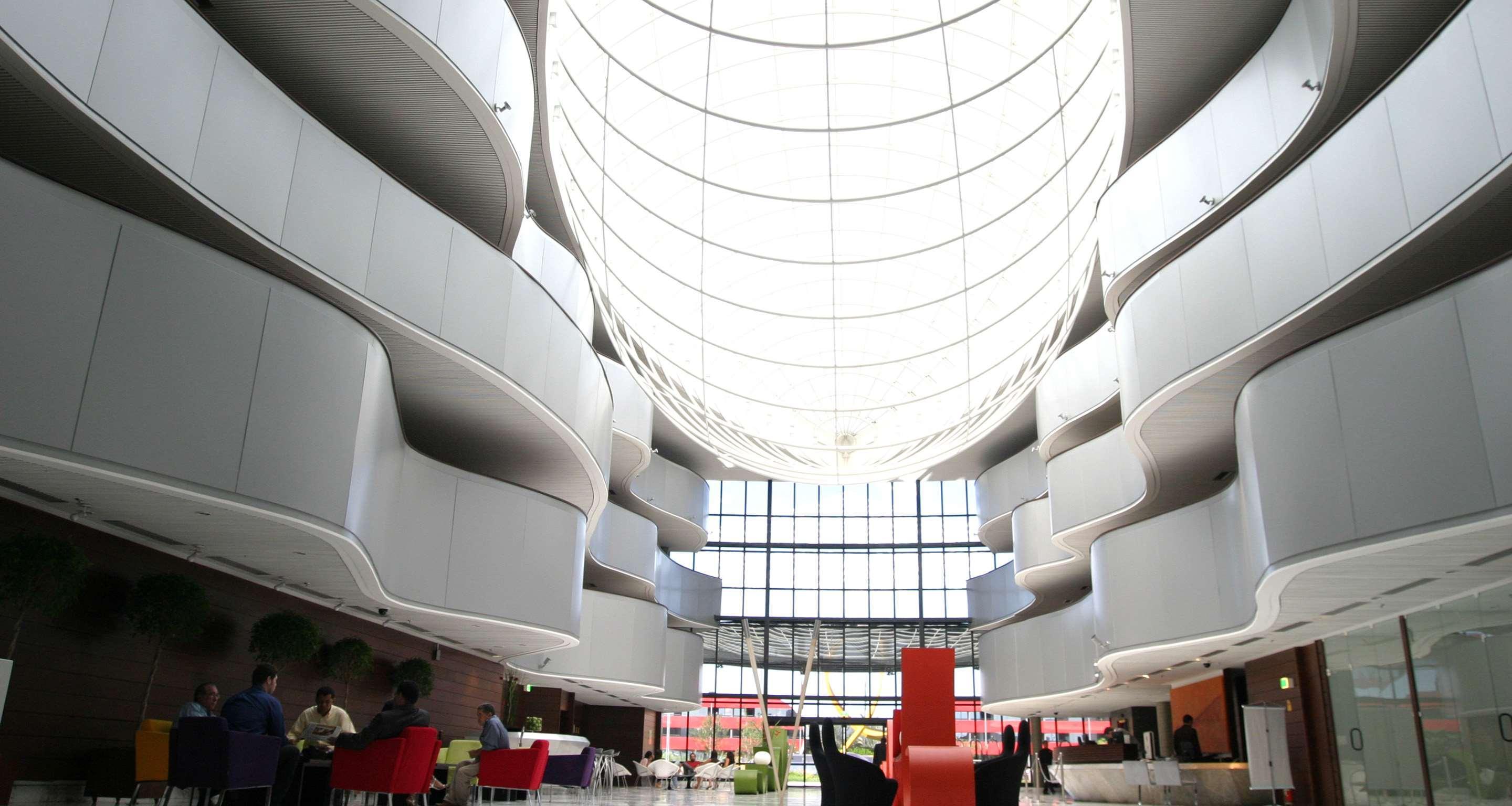 Royal Tulip Brasilia Alvorada Hotel ภายนอก รูปภาพ The photo depicts a modern interior space characterized by sleek, curvilinear architecture. The ceiling features a large, dome-like skylight that allows natural light to flood the area. The walls display a minimalist design with smooth, white surface