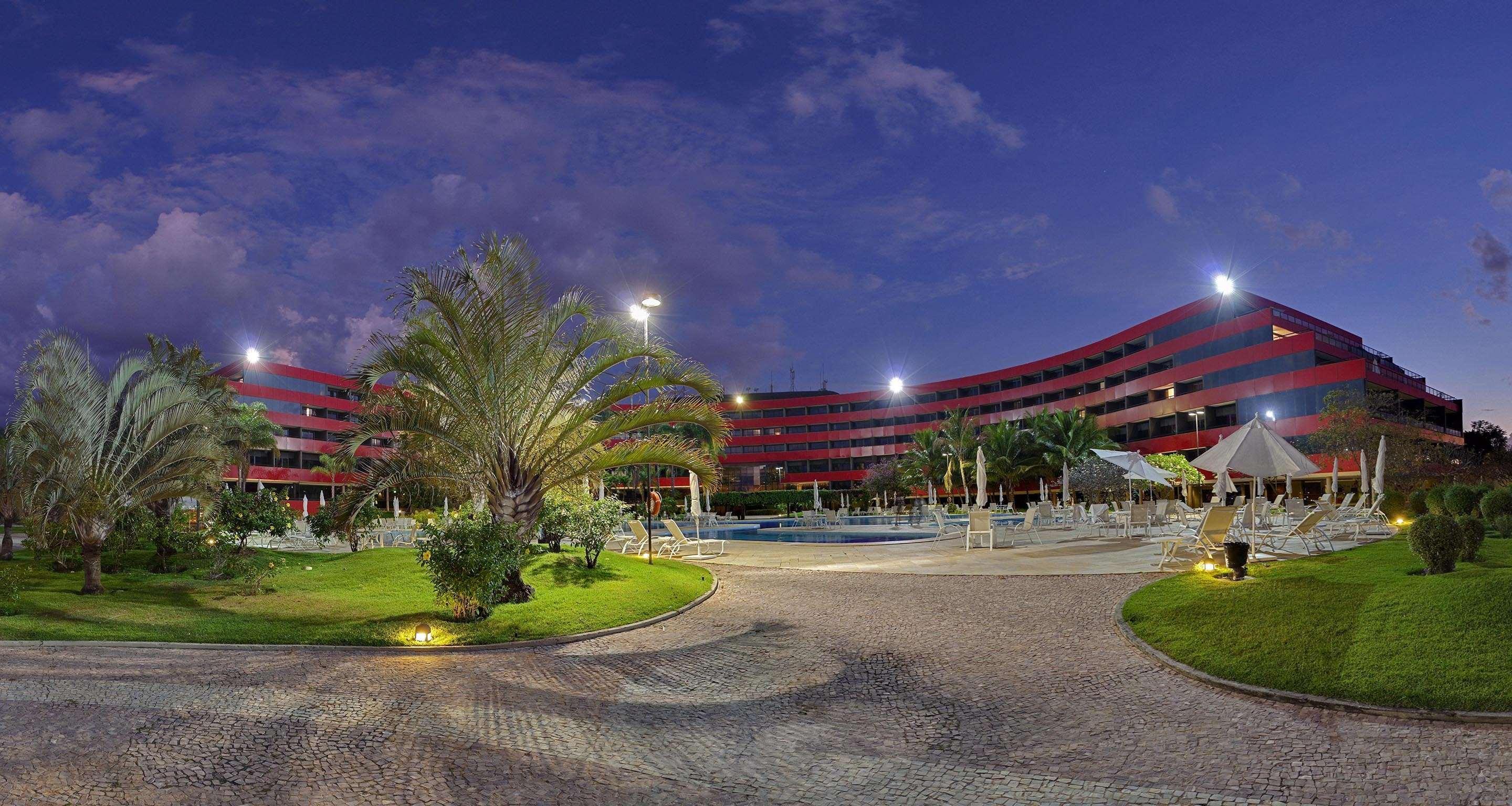 Royal Tulip Brasilia Alvorada Hotel ภายนอก รูปภาพ The photo shows a panoramic view of a hotel or resort complex, characterized by its modern architectural design with smooth, curved lines and a vibrant red color. It’s set in a landscaped area featuring palm trees and green grass. The surroundings in